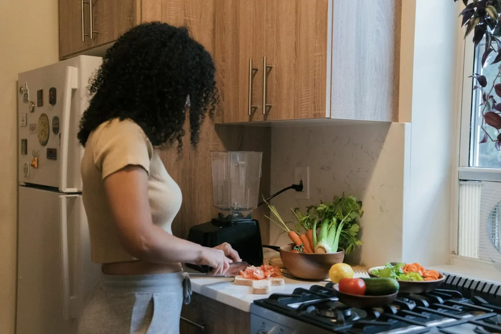 Slimmit食事對抗酵素膠原凍怎麼吃?正確食用方法與最佳時機 5 A woman cuts vegetables on a board in a modern kitchen setting, surrounded by fresh produce.