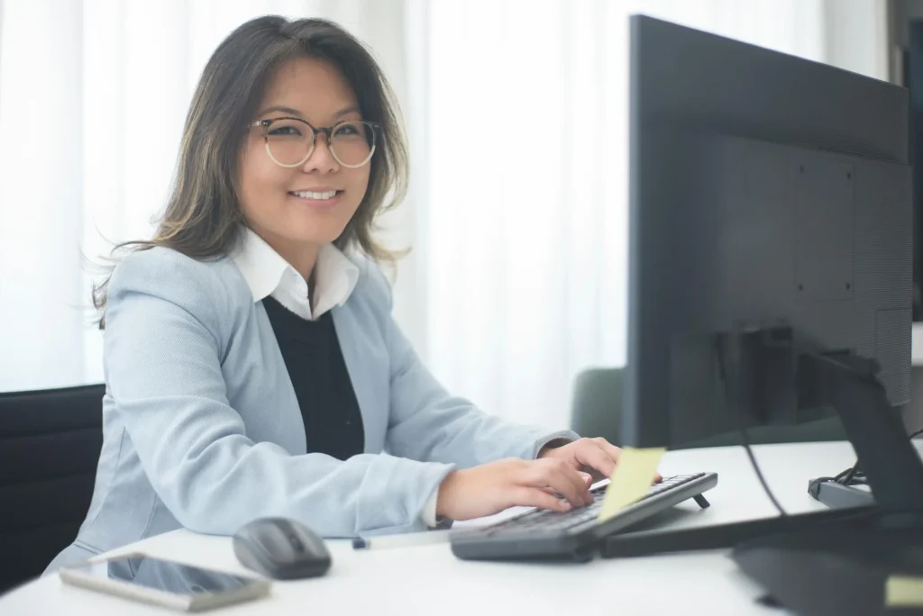 Slimmit酵素膠原凍真實評價 5 Professional woman smiling while working at a computer in an office setting.