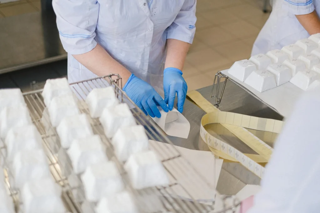 Slimmit食事對抗酵素膠原凍台灣HACCP工廠生產:從原料到成品的品質把關 8 Close-up of hands in blue gloves wrapping cheese blocks in an indoor setting.