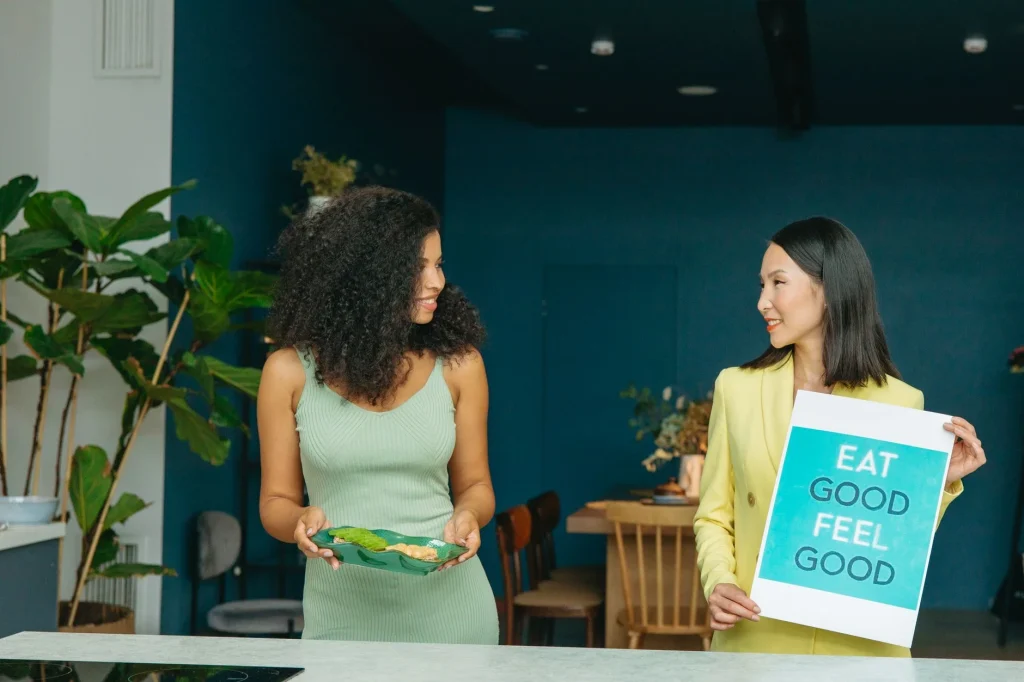 Slimmit食事對抗酵素膠原凍可以長期吃嗎?營養師專業建議 6 Two women discussing healthy eating with a sign and vegetables.